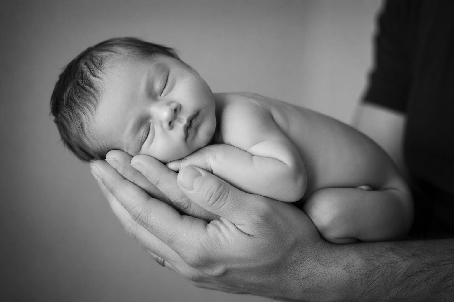 Newborn baby resting peacefully in caring hands in a black-and-white portrait.